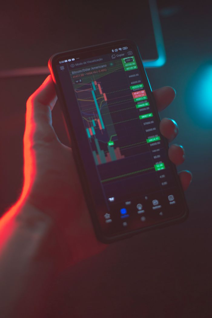 services-01 Close-up of a hand holding a smartphone with stock market data on the screen in a dimly lit environment.