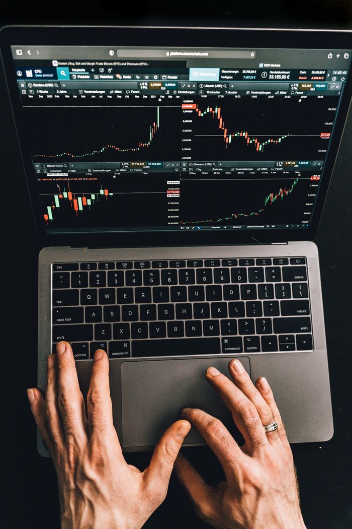 about-02 Close-up of hands using a laptop displaying stock market charts.