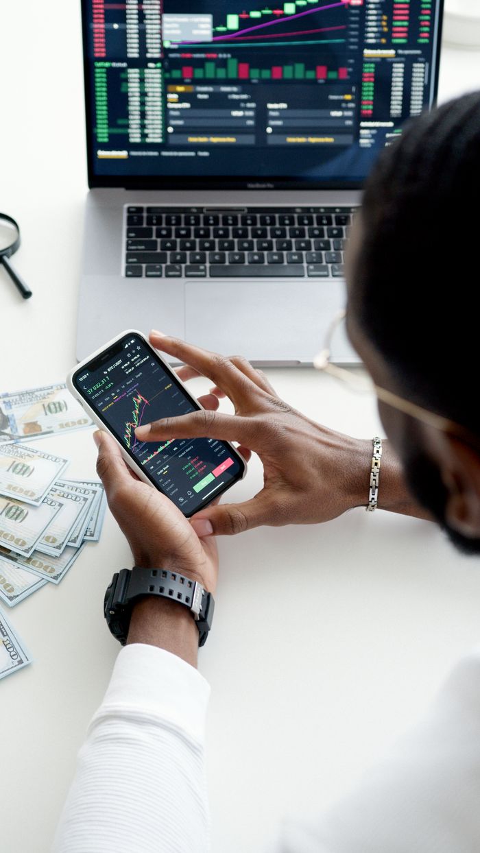 about-img A person trading stocks using a smartphone, showcasing financial data on mobile and laptop screens.